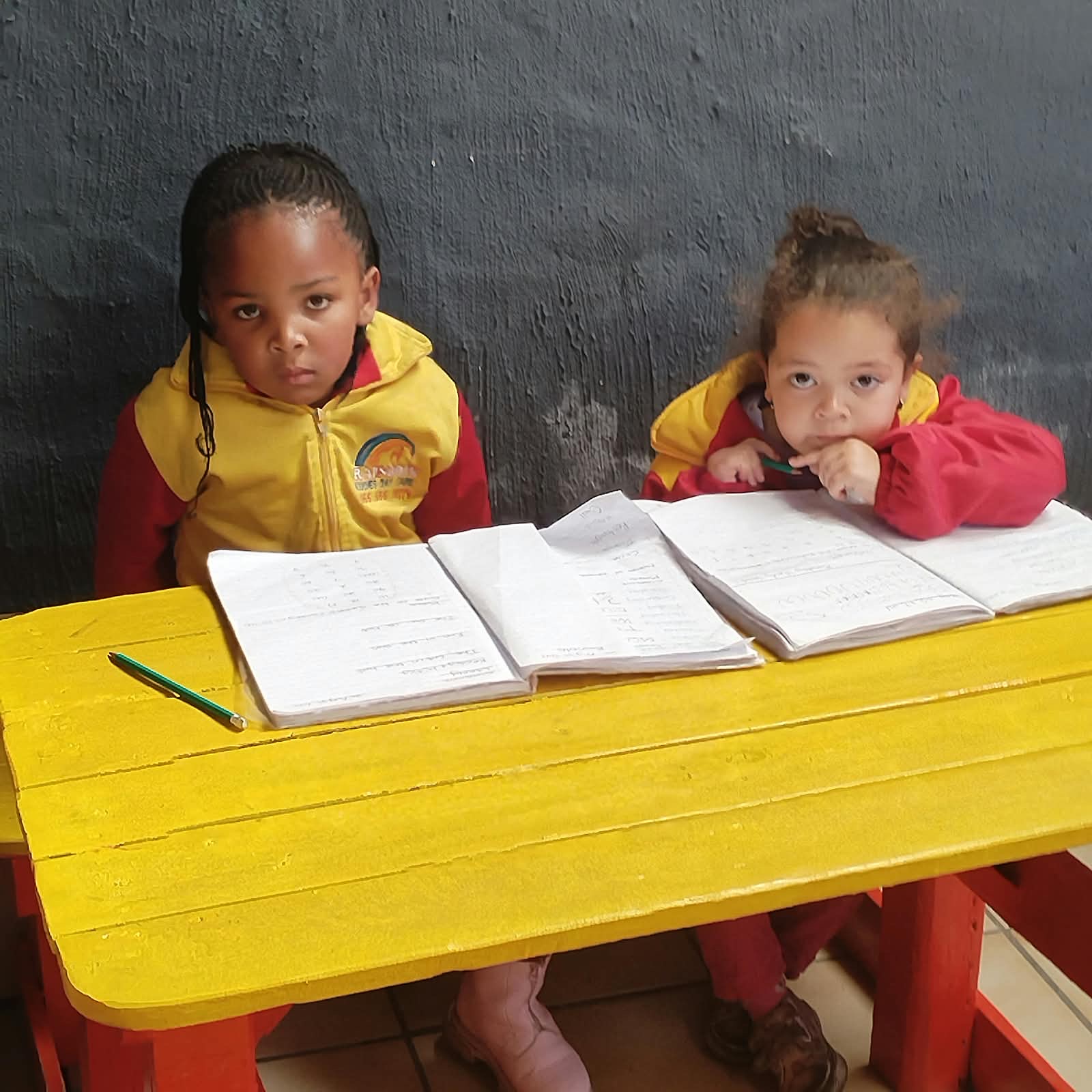 Two Rainbow Kiddies children with their school books at a yellow table